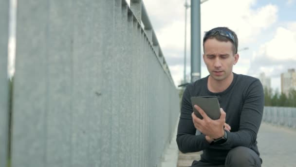 Portrait extérieur de jeune homme moderne avec tablette numérique. Garde-corps du pont, près de la route et les beaux nuages bleus en arrière-plan — Video