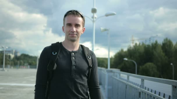 Joven hombre guapo en una buena ropa adecuada quita y lleva gafas de sol y sonrisa. paisaje urbano — Vídeos de Stock