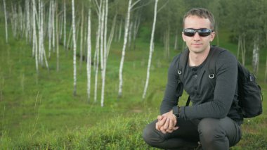 Genç yakışıklı adam bir güzel uygun giysiler içinde kaldırır ve güneş gözlüğü takıyor. Kamera, doğal manzara smile