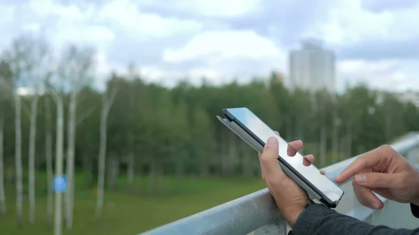 Dijital tablet ile modern genç adam açık portresi. Arka plan yeşil ağaçlar ve güzel mavi bulutlar karşı. Yakın çekim