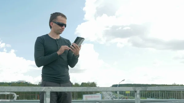 Dijital tablet ile modern genç adam açık portresi. Köprüde bir gözlük. Mavi gökyüzü