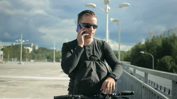 Erkek bisikletçi teleofon çağrısı nedeniyle sokak ve durdu aşağı sürme. O çanta cevaplar telefonu alır. Arka planda fırtına öncesi güzel gökyüzü