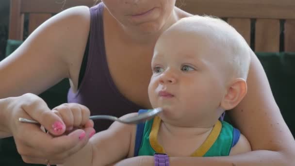 Karmienia dziecka Mama piękne zupa w kawiarni. Dzieciak lizanie łyżka nadal chce jeść. Blond chłopiec w zielony t-shirt — Wideo stockowe