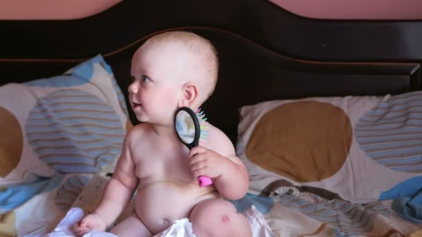 ベッドの上で櫛で遊ぶ美しい赤ちゃん。笑顔と櫛自体をしようとします。キッド1年。櫛の上に鏡がある — ストック動画