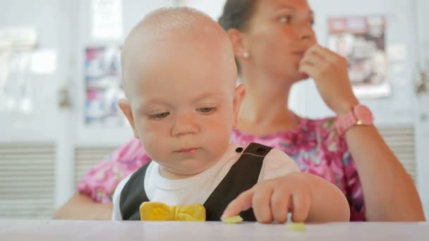 Mama i dziecko w pięknej sukni z motyla jeść w kawiarni na ulicy. Dziecko jedzą kawałek Sałatka ogórek matka — Wideo stockowe