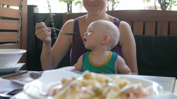 A fiatal anya az olaszországi tésztájából eteti a babát. Gyerek 1 év, zöld pólóban van. — Stock videók