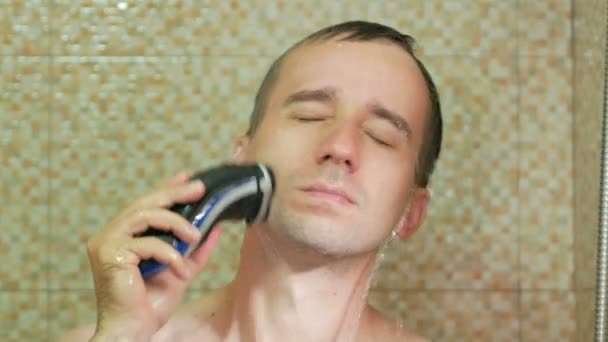 Muž, který se sprchne a holí s elektrickým břitvou. Vodotěsná rotační břitva v akci
