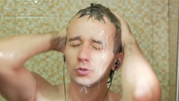 A man taking a shower at the hotel and listens to music on headphones. He loudly sings and enjoys wash — Stock Video