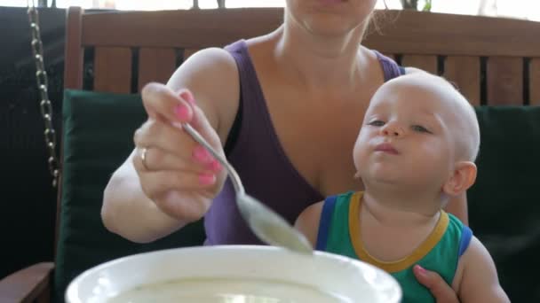 妈妈喂养宝宝美丽汤在咖啡馆里。孩子舔勺子还想吃。穿着绿色 t 恤的金发男孩 — 图库视频影像