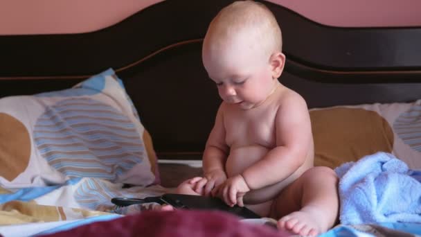 Hermoso bebé jugando con una tableta en la cama. Sonríe y trata de abrir la cubierta. Niño 1 año . — Vídeos de Stock