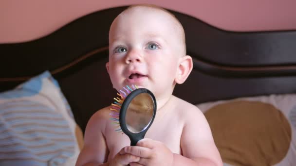 Beau bébé jouant avec peigne sur le lit. Souriez et essayez de vous peigner. Enfant 1 an. Sur le peigne est un miroir — Video