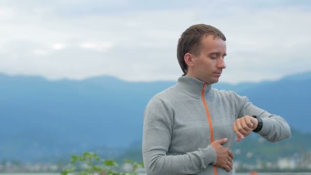 En man går längs stranden och kontrollera meddelanden på smarta klockan nära havet. Han är ansvarig i sociala nätverk — Stockvideo