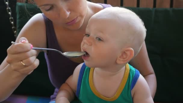 Moeder voeding baby mooi soep in het café. Jongen likt de lepel nog wil eten. Blonde jongen in een groen t-shirt — Stockvideo