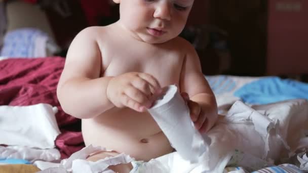 Atractivo bebé sentado en una cama y rasgando papel higiénico. Niño 1 año — Vídeo de stock