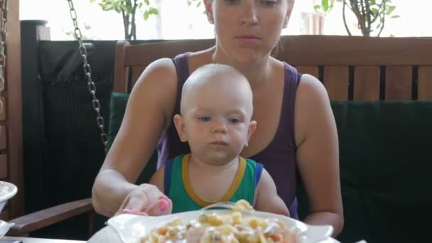 Молодая мама кормит ребенка пастой для коленей в Италии. Ребенок 1 год, он в зеленой футболке — стоковое видео