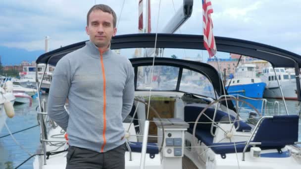 Beau jeune homme debout près de son yacht. Il regarde dans la caméra — Video