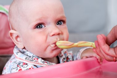 Güzel bebek anneler elinden püresi yiyor. O pembe çocuk sandalyede oturuyor.