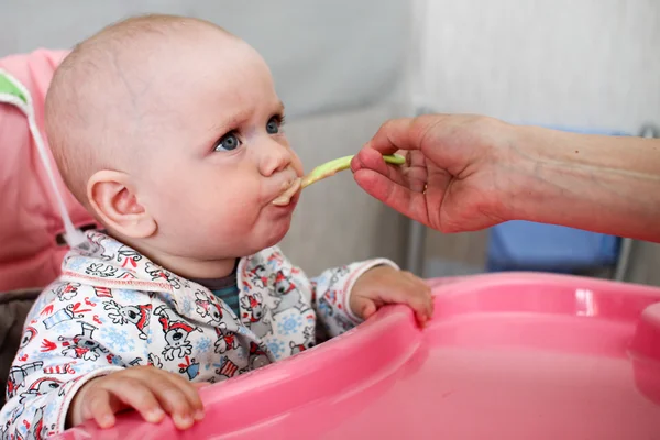 Hermoso bebé come gachas de la mano de las mamás. Está sentado en una silla rosa para niños. . — Foto de Stock