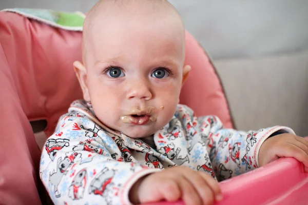 Hermoso bebé come gachas de la mano de las mamás. Está sentado en una silla rosa para niños. . — Foto de Stock