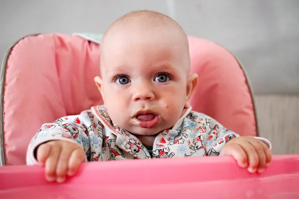 Hermoso bebé come gachas de la mano de las mamás. Está sentado en una silla rosa para niños. . — Foto de Stock