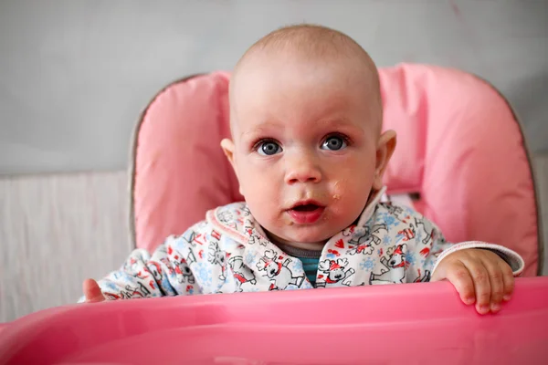 Красива дитина їсть кашу з рук мам. Він сидить на рожевому дитячому стільці . — стокове фото