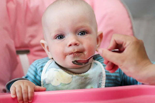 Hermoso bebé come gachas de la mano de las mamás. Está sentado en una silla rosa para niños. . — Foto de Stock