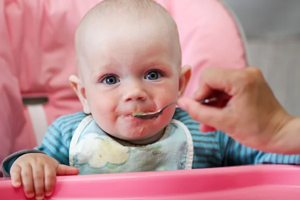 Hermoso bebé come gachas de la mano de las mamás. Está sentado en una silla rosa para niños. . — Foto de Stock