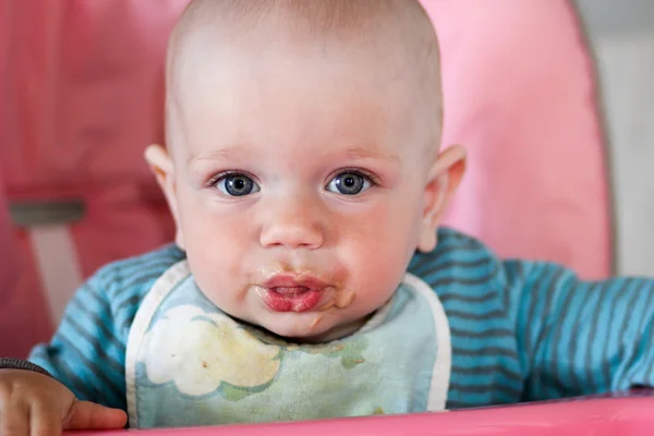 Mooie baby eet PAP uit moeders hand. Hij zit op een kinderstoel roze. — Stockfoto