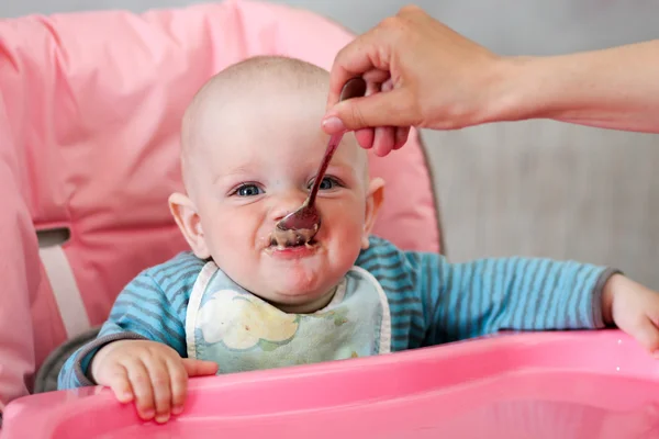 Hermoso bebé come gachas de la mano de las mamás. Está sentado en una silla rosa para niños. . — Foto de Stock