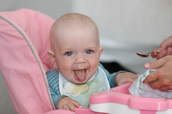 Hermoso bebé come gachas de la mano de las mamás. Está sentado en una silla rosa para niños. . — Foto de Stock