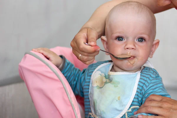 Hermoso bebé come gachas de la mano de las mamás. Está sentado en una silla rosa para niños. . — Foto de Stock