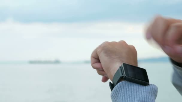 Mano maschile sfogliare i messaggi sull'orologio intelligente. Sullo sfondo oceano sfocato e nuvole. La nave trasporta carichi. Primo piano — Video Stock