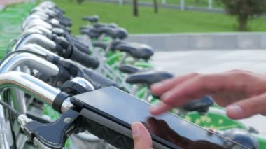 Bir adam bir bisiklet park yeri Tablet PC'de iletilerde denetler. Bir bisiklet kiralayıp olacak hes