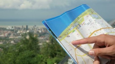 Yüksek katlı binalar ve sıradan evler ile modern bir şehir. Bir adam bir kağıt harita rotasında denetler. Orman ve deniz arkasında