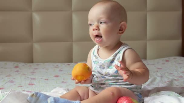 Ein hübsches Baby isst einen Pfirsich auf einem Frühstück im Bett. er reißt ein Stück ab und steckt es in den Mund — Stockvideo