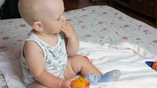 Un bebé guapo comiendo un melocotón en un desayuno en la cama. Le arranca un pedazo y se lo mete en la boca. — Vídeo de stock