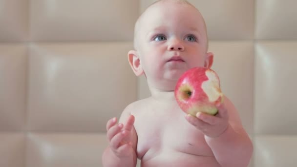 Een knappe baby eet een appel in bed bij het ontbijt. Hij bijt uit een stuk en zet in zijn mond — Stockvideo
