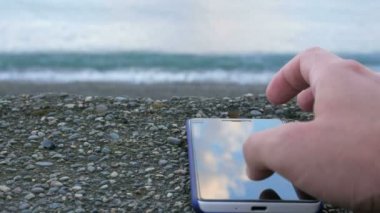 Okyanus çakıl plajı hakkında cep telefonudur. Fotoğraflarınızı için görünen adam. Yakın çekim.