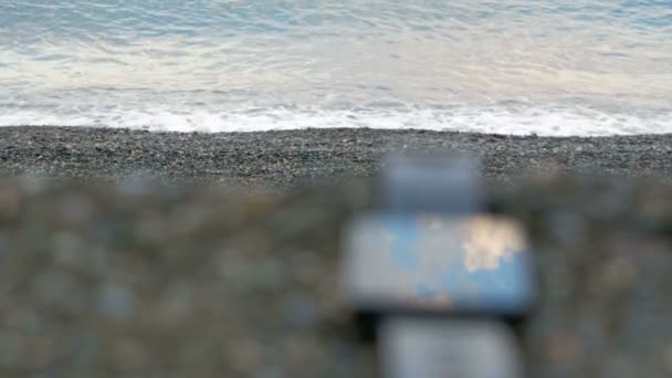 Relógios inteligentes desfocados estão perto da praia de seixos do oceano. O relógio reflete as nuvens do céu. Close-up . — Vídeo de Stock