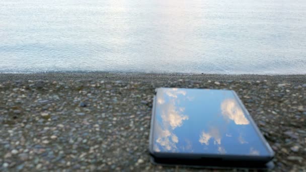 O telemóvel é sobre a praia de seixos do oceano. Ondas calmas batendo contra a costa. conceito de Telecomunicações — Vídeo de Stock