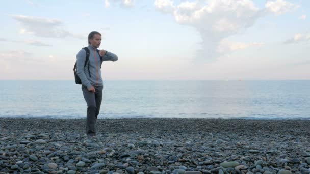 Un homme marche le long de la plage et vérifie les messages sur la montre intelligente près de l'océan. Il est responsable dans les réseaux sociaux — Video