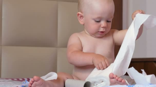 Aantrekkelijke baby zittend op een bed en tearing van wc-papier. Kind 1 jaar — Stockvideo