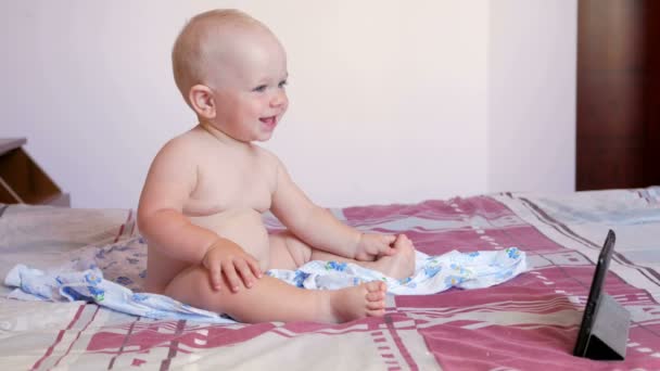 Słodkie dziecko siedząc na łóżku i patrzy bajki na tablecie Pc. Tiny rok dziecka z nie ubrania — Wideo stockowe