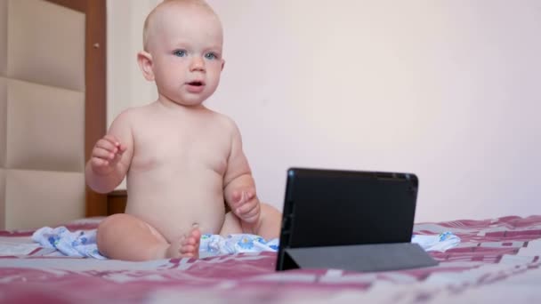 Roztomilé dítě sedí na posteli a pohledy karikatury, na tabletu Pc. Tiny roční dítě bez oblečení