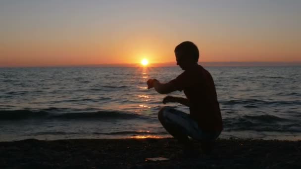 Silhouette Mann mit Smartwatch in der Hand am Strand bei Sonnenuntergang. Er berührt die Smartwatches und checkt die Nachricht. die Sonne ist fast hinter dem Ozean untergegangen. — Stockvideo