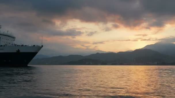 Large ship sailing into the port at sunrise over the ocean. Mountains and orange sun against the background of the ship. cargo carriage concept — Stock Video