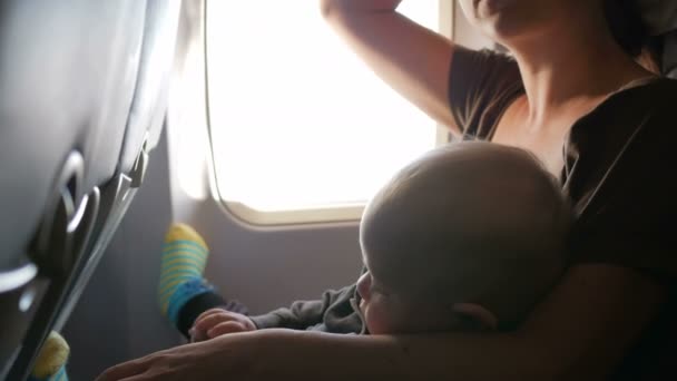 Дитина сидить на матерях на колінах на літаку під час польоту. Він дивиться навколо і торкається пояса . — стокове відео