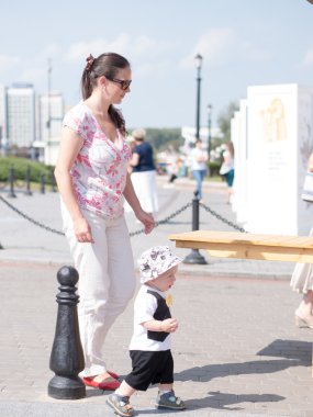 Güzel yürümeye başlayan çocuk annesi ile bir şehir tatile yürüme. Şık giyimli kelebek ve kap evlat