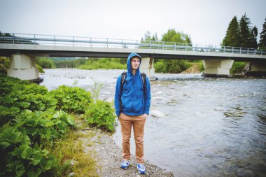 Erkek turist dağ nehrinin yanında duruyor.