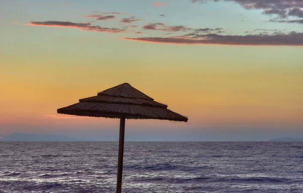 Straw beach umbrella on a background of the sea and the evening sky — Stock Photo, Image